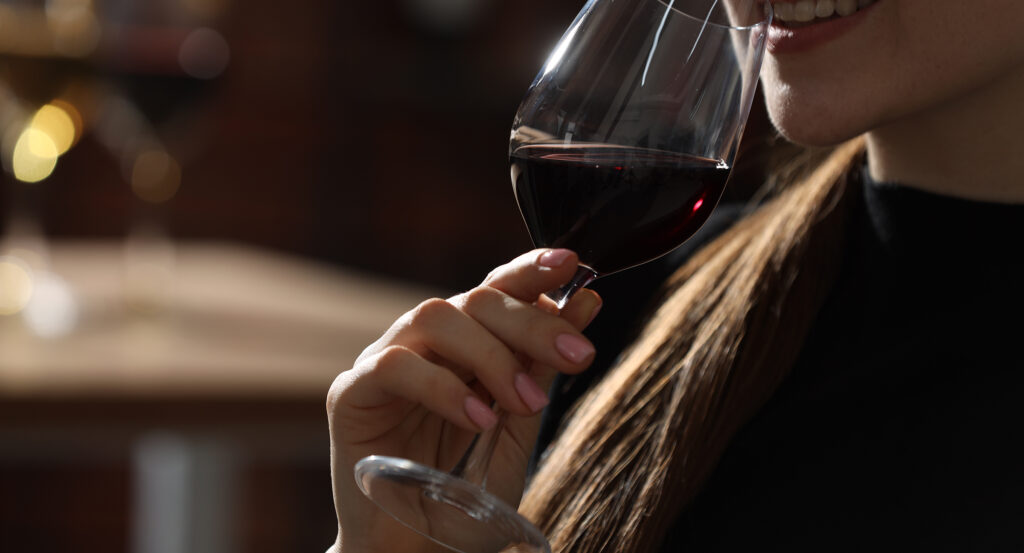 Woman with glass of red wine against blurred background, closeup. Space for text
